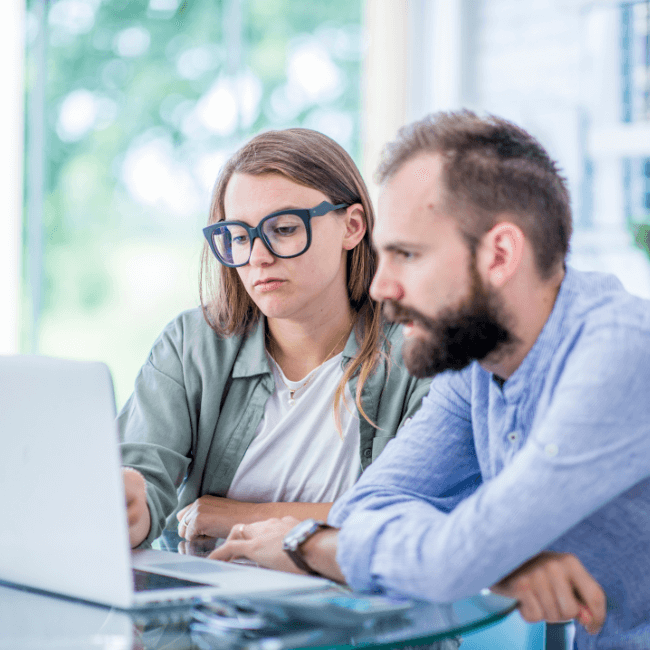 A couple sitting at a table looking at a laptop weighing up the pros and cons of buying or building a house