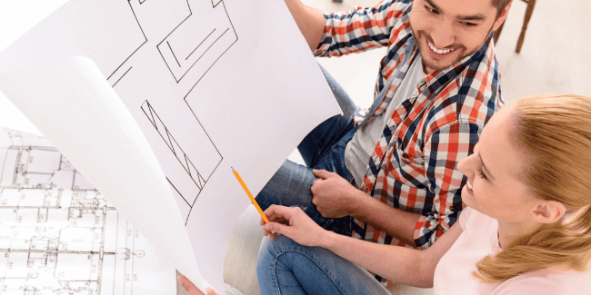 Two people sitting on the floor looking at their house plans. They're building their first home