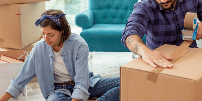 Selling-Your-House-How-to-Emotionally-Prepare image of a couple sitting in the lounge room packing boxes