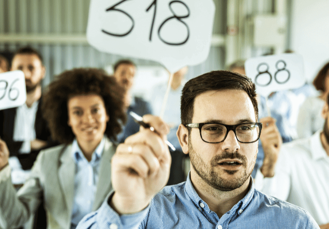 a group of people holding up their bidder numbers as they bid at a house auction